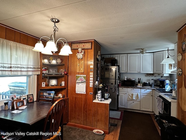 kitchen featuring wooden walls, electric stove, a notable chandelier, stainless steel refrigerator, and hanging light fixtures