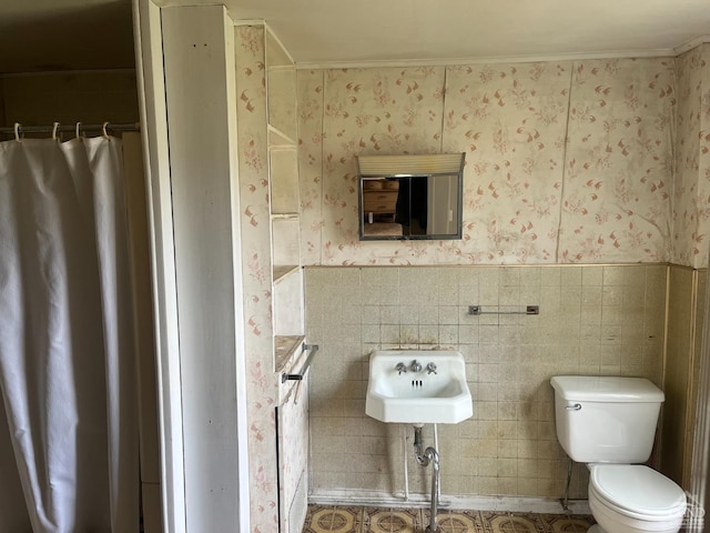 bathroom with toilet, wallpapered walls, a sink, wainscoting, and a shower with curtain