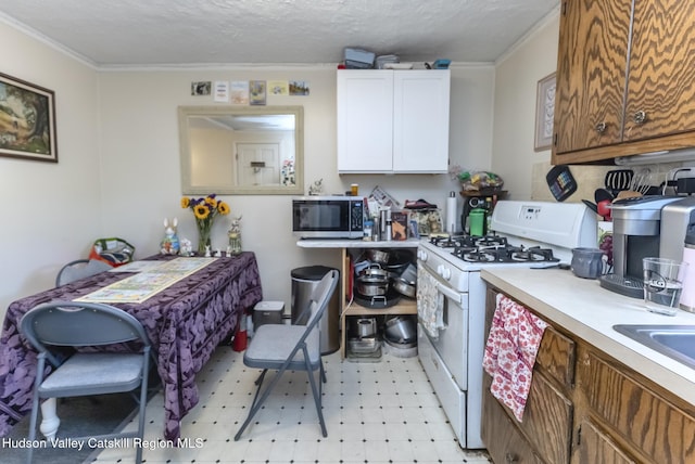 kitchen with crown molding, light countertops, white gas range oven, stainless steel microwave, and white cabinetry