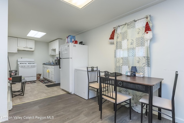 kitchen with white appliances, white cabinets, under cabinet range hood, and wood finished floors