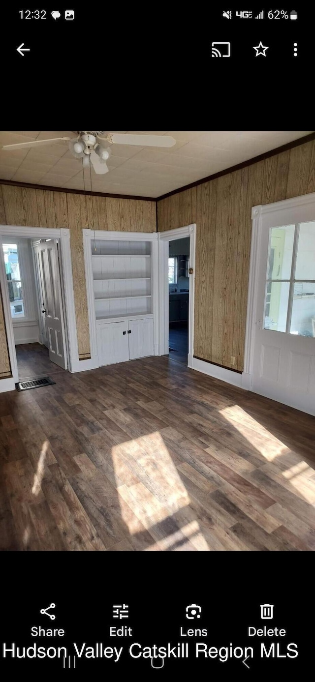 unfurnished living room featuring dark hardwood / wood-style floors, ceiling fan, and wooden walls