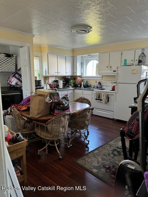 kitchen with white cabinetry, crown molding, dark wood-type flooring, and white appliances