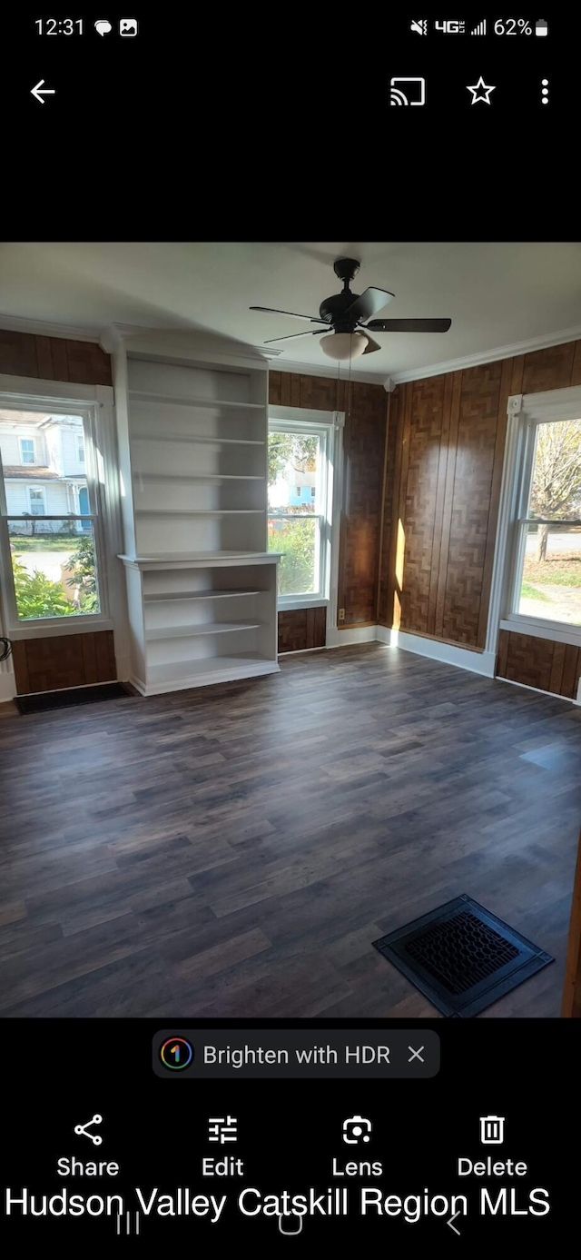 unfurnished living room with wood walls, dark hardwood / wood-style flooring, ceiling fan, and a healthy amount of sunlight