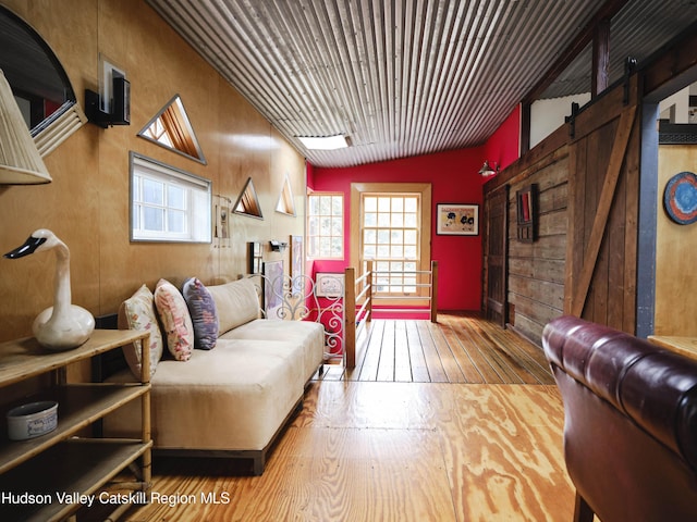 living room with wood-type flooring, a barn door, vaulted ceiling, and wood walls