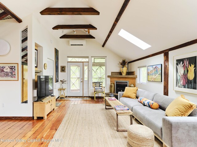 living room featuring light wood-type flooring, a wall unit AC, and vaulted ceiling with skylight