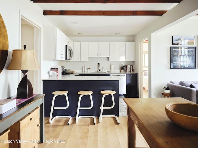 kitchen featuring white cabinets, sink, light hardwood / wood-style flooring, beamed ceiling, and stainless steel appliances