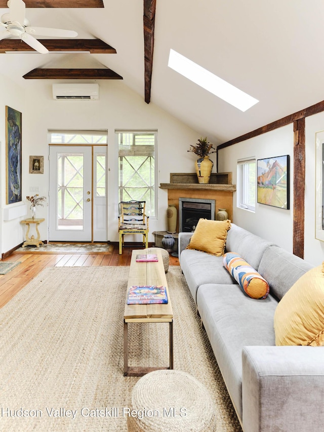 living room with hardwood / wood-style flooring, ceiling fan, a wall mounted air conditioner, and lofted ceiling with skylight