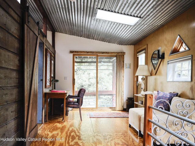 bedroom featuring a barn door, light wood-type flooring, and lofted ceiling