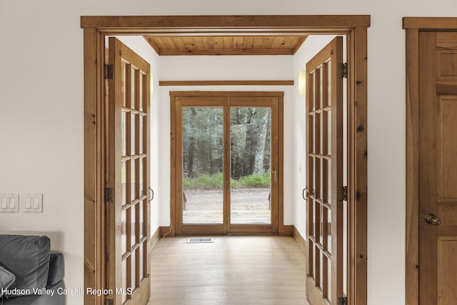 doorway with beamed ceiling, light wood finished floors, wooden ceiling, baseboards, and visible vents