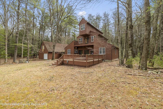 back of property with an outbuilding, a forest view, a balcony, and a deck