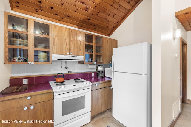 kitchen featuring vaulted ceiling, tile counters, extractor fan, white appliances, and backsplash