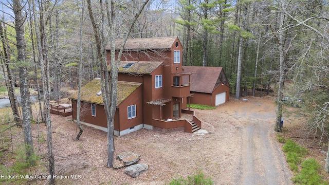 view of side of home with a garage, a shingled roof, dirt driveway, a forest view, and crawl space