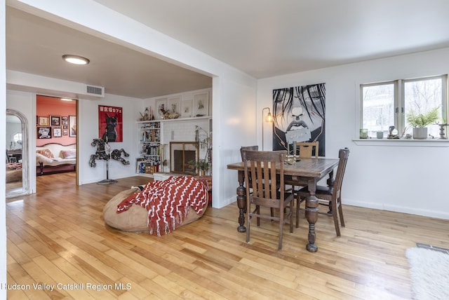 dining area featuring visible vents, a brick fireplace, baseboards, and wood-type flooring