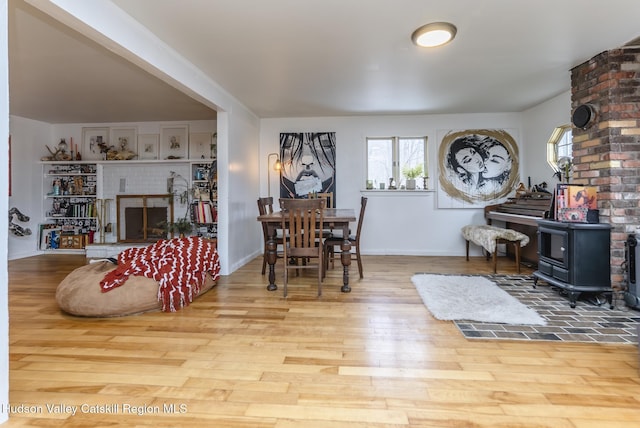 dining space featuring a fireplace, a wood stove, wood finished floors, and baseboards