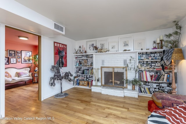 living area with visible vents, a brick fireplace, and wood finished floors