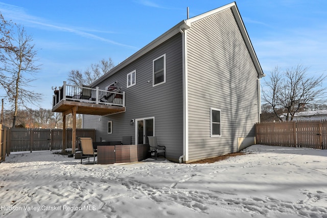 snow covered back of property with a balcony and a hot tub