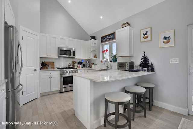 kitchen featuring kitchen peninsula, appliances with stainless steel finishes, a kitchen breakfast bar, high vaulted ceiling, and white cabinets