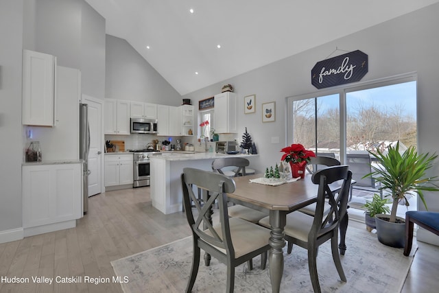 dining room featuring light hardwood / wood-style floors, high vaulted ceiling, and sink