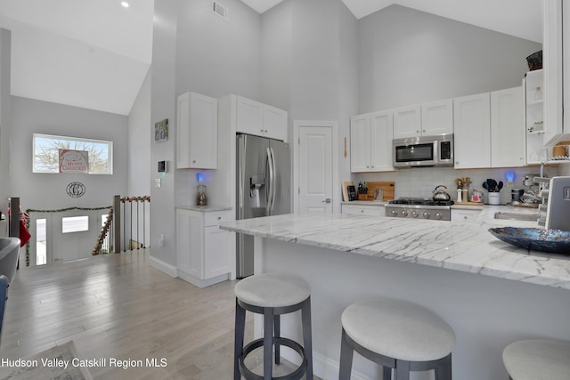 kitchen featuring white cabinets, stainless steel appliances, high vaulted ceiling, and a breakfast bar area