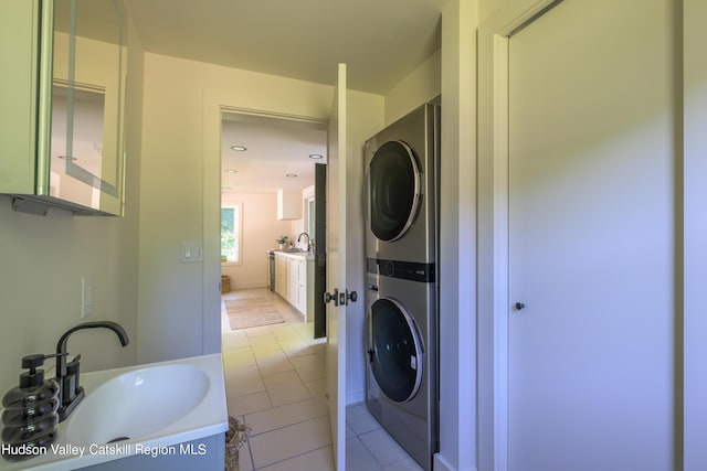 laundry area with sink, light tile patterned floors, and stacked washer and clothes dryer