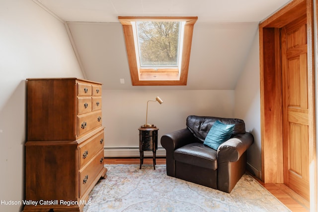 sitting room featuring light wood-type flooring, lofted ceiling with skylight, and a baseboard heating unit