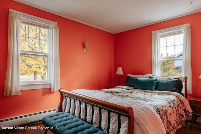 bedroom featuring multiple windows, wood-type flooring, and a baseboard heating unit