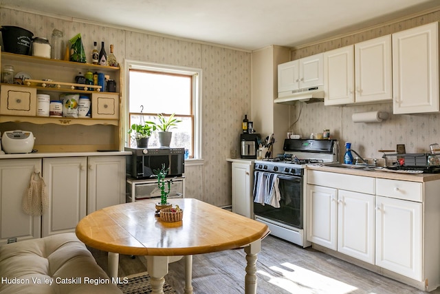 kitchen with wallpapered walls, under cabinet range hood, range with gas stovetop, light wood finished floors, and a sink