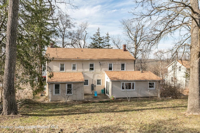 back of house featuring a patio, a chimney, and a lawn