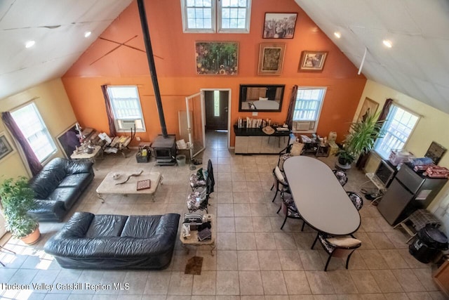 living room featuring a wood stove, high vaulted ceiling, and light tile patterned flooring