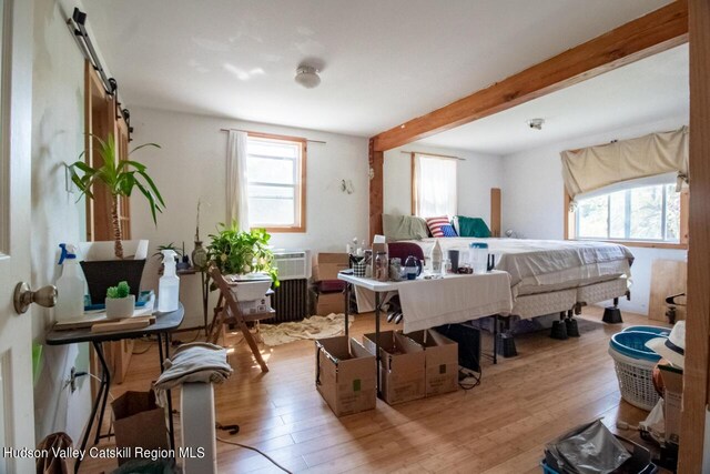 bedroom featuring light hardwood / wood-style floors, a barn door, beam ceiling, and multiple windows