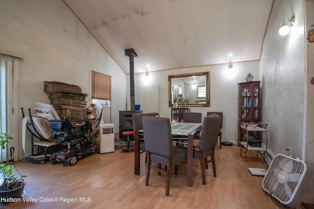 dining area with a wood stove, light hardwood / wood-style floors, and lofted ceiling