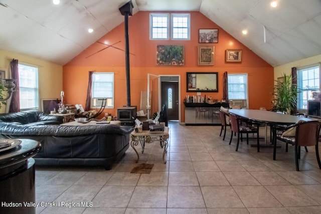 tiled living room featuring plenty of natural light, a wood stove, and high vaulted ceiling