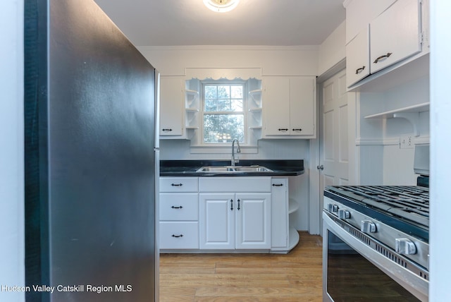 kitchen featuring appliances with stainless steel finishes, ornamental molding, sink, light hardwood / wood-style flooring, and white cabinetry