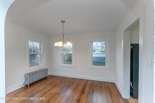 spare room featuring wood-type flooring, radiator heating unit, and an inviting chandelier