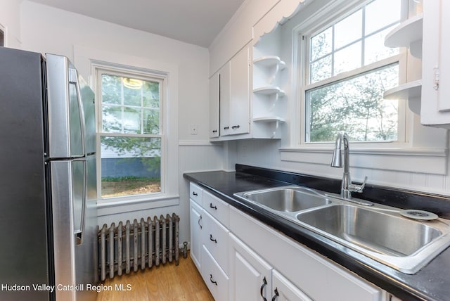 kitchen featuring white cabinetry, a wealth of natural light, sink, radiator heating unit, and stainless steel fridge