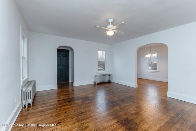 spare room featuring ceiling fan with notable chandelier, radiator, and dark wood-type flooring