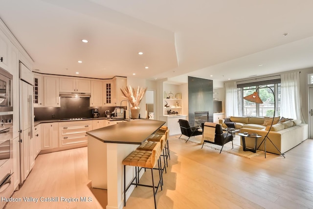 10 Enclave N Dr Unit 106, Windham, NY 12496 - kitchen with dark countertops, a kitchen bar, light wood finished floors, glass insert cabinets, and stainless steel appliances