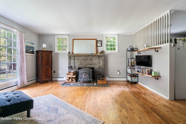 living room with a wood stove, hardwood / wood-style floors, a healthy amount of sunlight, and a baseboard heating unit