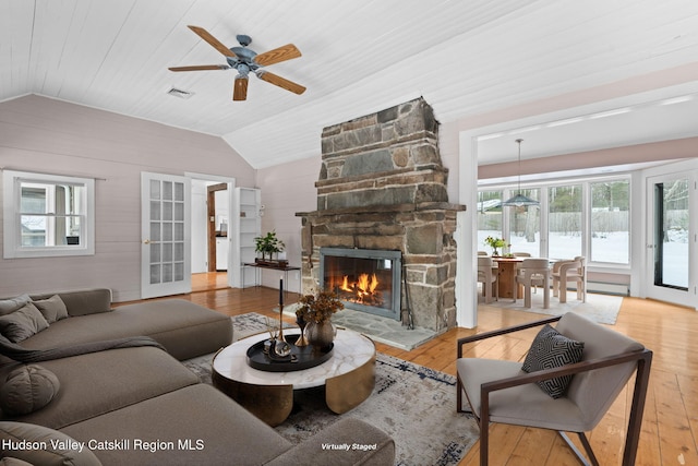 living room with vaulted ceiling, a stone fireplace, ceiling fan, wooden ceiling, and light hardwood / wood-style flooring