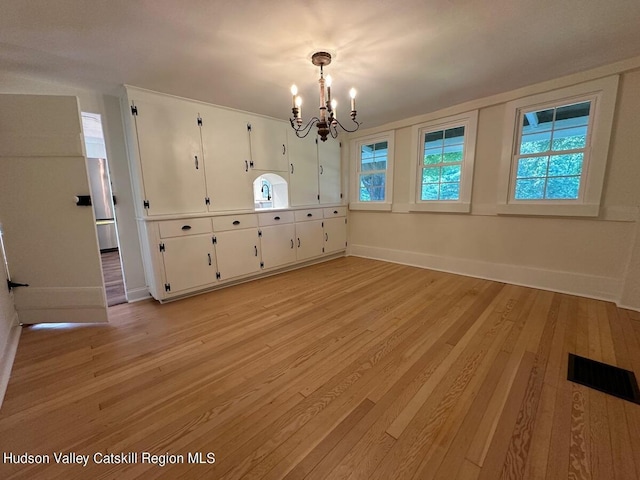 unfurnished dining area with a healthy amount of sunlight, light wood-type flooring, and an inviting chandelier