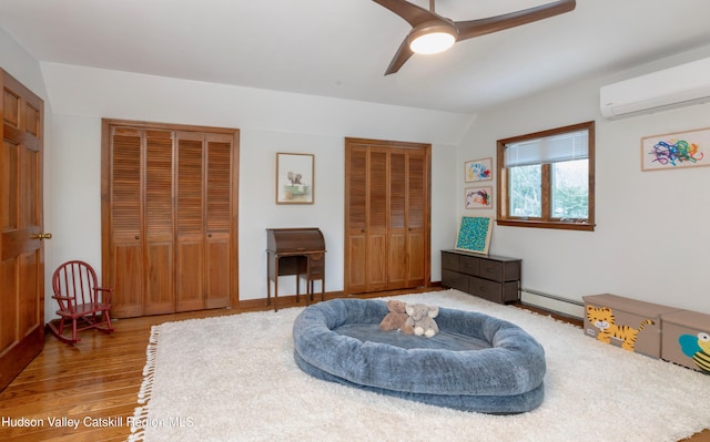 sitting room featuring a wall mounted air conditioner, wood-type flooring, lofted ceiling, ceiling fan, and baseboard heating