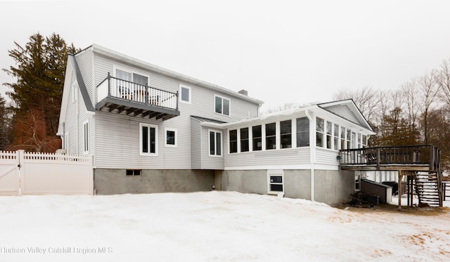 snow covered back of property featuring a balcony and a sunroom