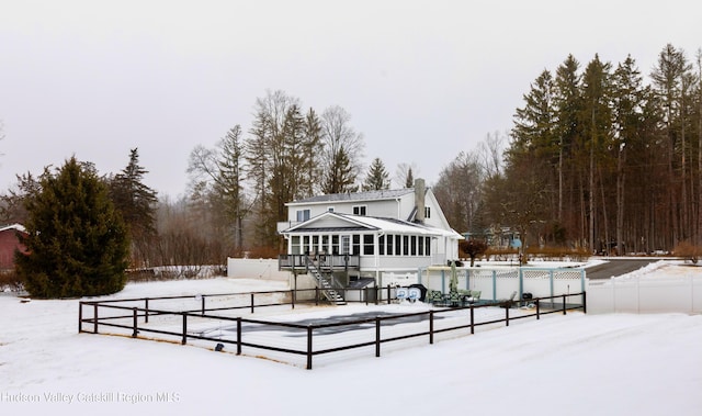 snow covered rear of property featuring a sunroom