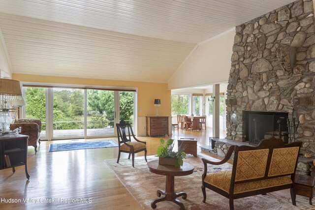 interior space with crown molding, a stone fireplace, high vaulted ceiling, and light wood-type flooring