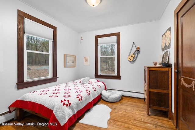 bedroom with multiple windows, light hardwood / wood-style flooring, and baseboard heating