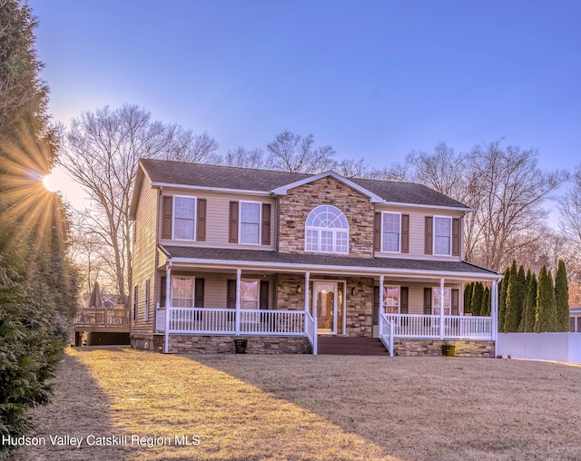 view of front of home featuring stone siding, covered porch, a front yard, and fence