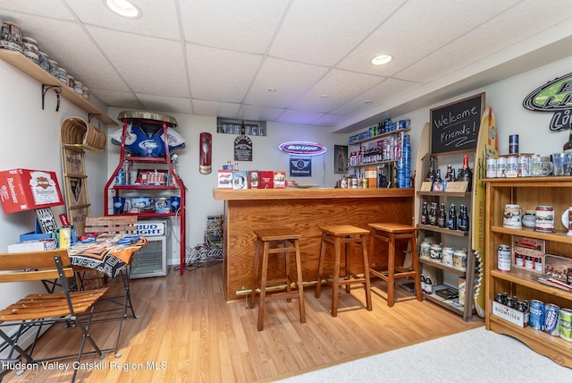 bar with a bar, a paneled ceiling, and wood finished floors