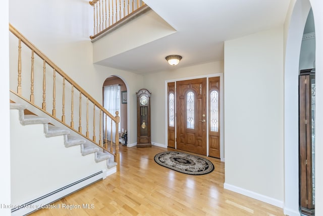 entrance foyer featuring baseboards, stairs, baseboard heating, wood finished floors, and arched walkways