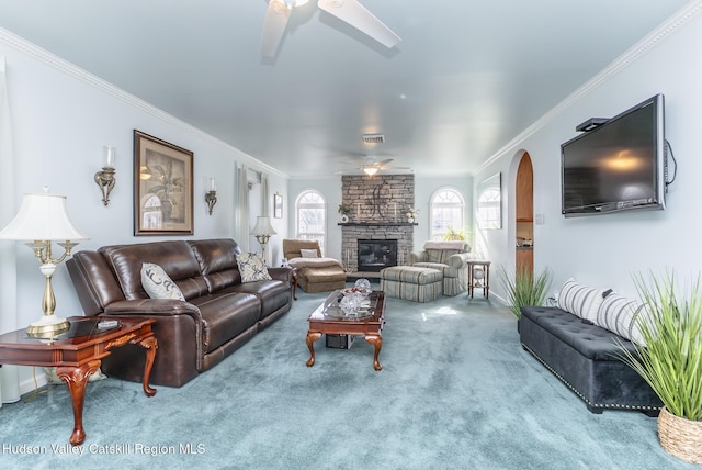 carpeted living room with visible vents, a fireplace, arched walkways, ceiling fan, and crown molding