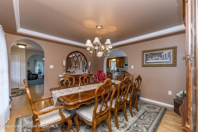 dining area with arched walkways, a chandelier, and light wood-type flooring